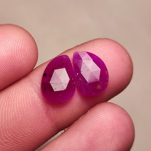 May include: Two faceted pink ruby gemstones in a pear shape.