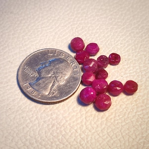 May include: A group of small, faceted ruby red gemstones, approximately the size of a UK 20 pence coin.