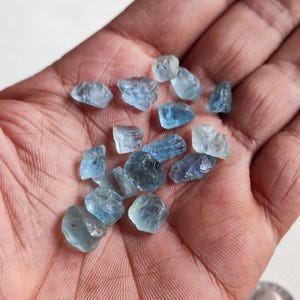 Pu&ograve; includere: Una collezione di piccoli cristalli di acquamarina grezzi di colore blu chiaro. I cristalli sono di varie forme e dimensioni e hanno un aspetto traslucido.