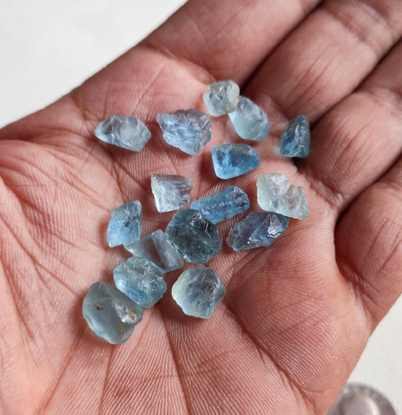 Pu&ograve; includere: Una collezione di piccoli cristalli di acquamarina grezzi di colore blu chiaro. I cristalli sono di varie forme e dimensioni e hanno un aspetto traslucido.