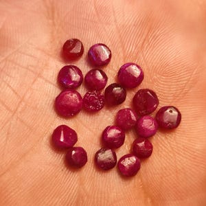 May include: A collection of 17 faceted ruby gemstones in various sizes and shapes, displayed on a hand.