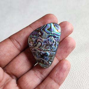 Op de afbeelding: Een iriserende abalone schelp cabochon met een driehoekige vorm en een blauw, groen en paars kleurenschema.