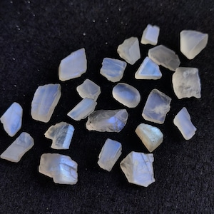 May include: A collection of iridescent moonstone crystals in various shapes and sizes. The crystals are a milky white color with a blue sheen.