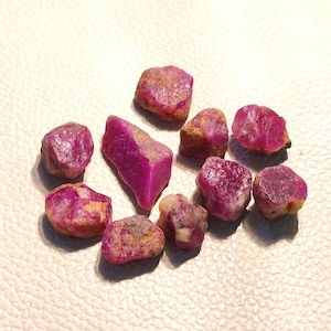 Puede incluir: Una colección de diez pequeñas piedras preciosas de rubí rosa en bruto. Las piedras preciosas son de varias formas y tamaños.