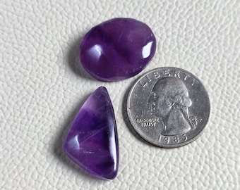 May include: Three amethyst gemstones, two are oval shaped and one is triangular. The gemstones are purple and have a shiny finish. A US quarter is included for size reference.
