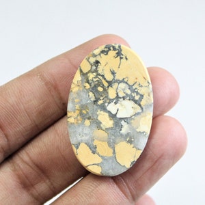 May include: A yellow and gray oval cabochon gemstone with a unique marbled pattern. The stone has a smooth, polished surface.