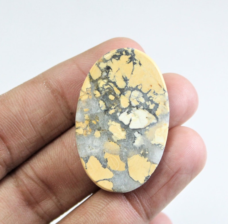 May include: A yellow and gray oval cabochon gemstone with a unique marbled pattern. The stone has a smooth, polished surface.