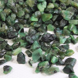 Op de afbeelding: Een verzameling ruwe, groene smaragd edelstenen. De smaragden zijn van verschillende groottes en vormen, sommige hebben een donkerdere, bijna zwarte insluiting.