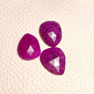 May include: Three faceted purple gemstone cabochons in a teardrop shape.