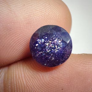 以下が含まれることがあります： 深い紫色の丸いファセットカットの宝石で、キラキラと虹色に輝く仕上げになっています。