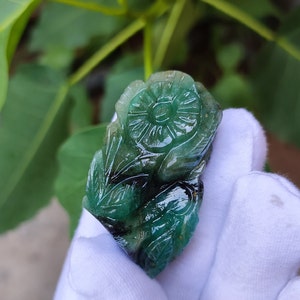 May include: A green emerald gemstone carved into a flower design. The flower has intricate details and is set against a white background.
