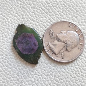 Op de afbeelding: Een groene en paarse edelsteen met een ruwe, onregelmatige vorm. De edelsteen is ongeveer zo groot als een Amerikaanse kwart.