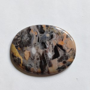 May include: Oval shaped cabochon of agate with a black, white, and orange pattern. The stone has a polished finish and is set in a silver tone setting.