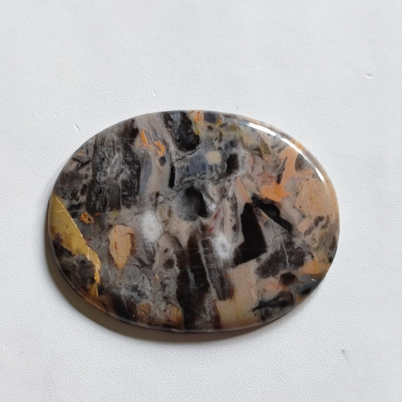 May include: Oval shaped cabochon of agate with a black, white, and orange pattern. The stone has a polished finish and is set in a silver tone setting.