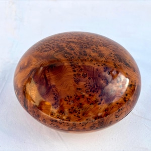 以下が含まれることがあります： 自然な木目仕上げの丸い木製の箱。箱は濃い茶色で赤みがかっており、光沢のある仕上げになっています。