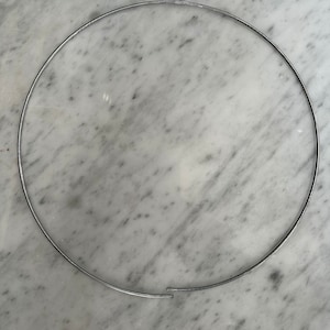 May include: A silver metal hoop, lying flat on a white marble surface.