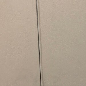 May include: A slender, silver-colored metal tool with a U-shaped top and a hooked bottom. The tool is straight and appears to be a specialized instrument, possibly for crafting or repair.