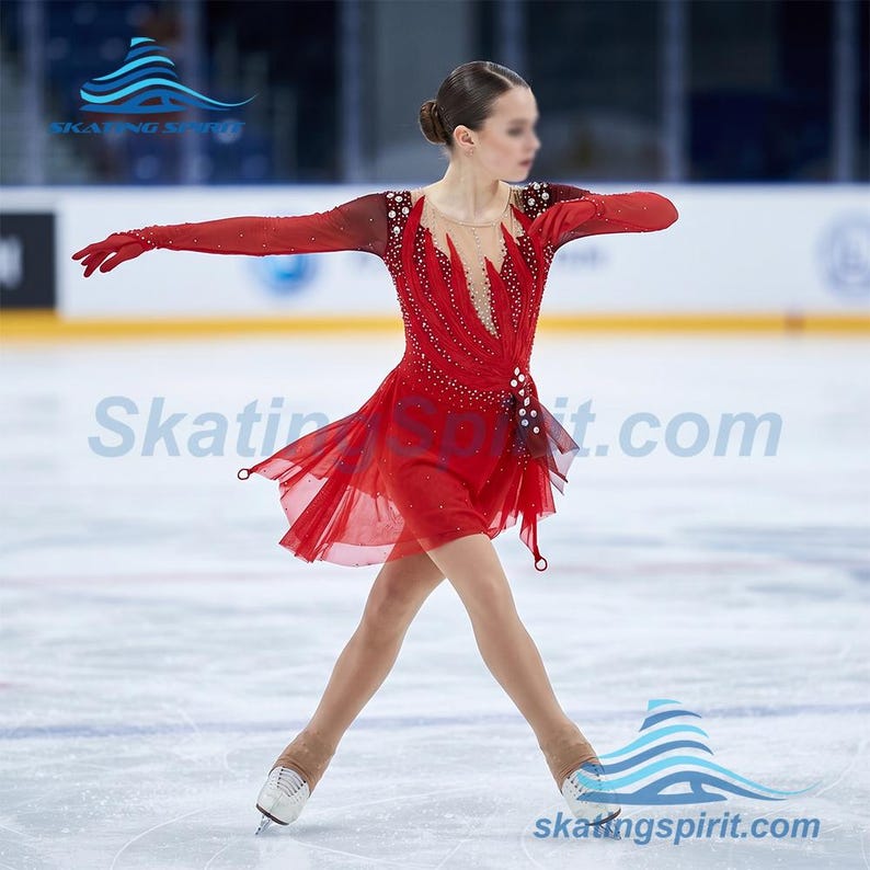 Peut inclure: Une robe de patinage artistique rouge vif avec des manches longues transparentes, un d&eacute;collet&eacute; en V profond avec un empi&egrave;cement en maille illusion et des ornements en cristal dispos&eacute;s en motif de flammes. La jupe est superpos&eacute;e et inclut des gants rouges.