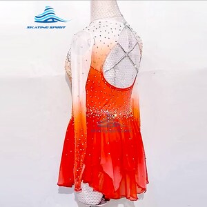 May include: Orange and white figure skating dress with long sleeves and a layered skirt. The dress is decorated with rhinestones and has a criss-cross back design.
