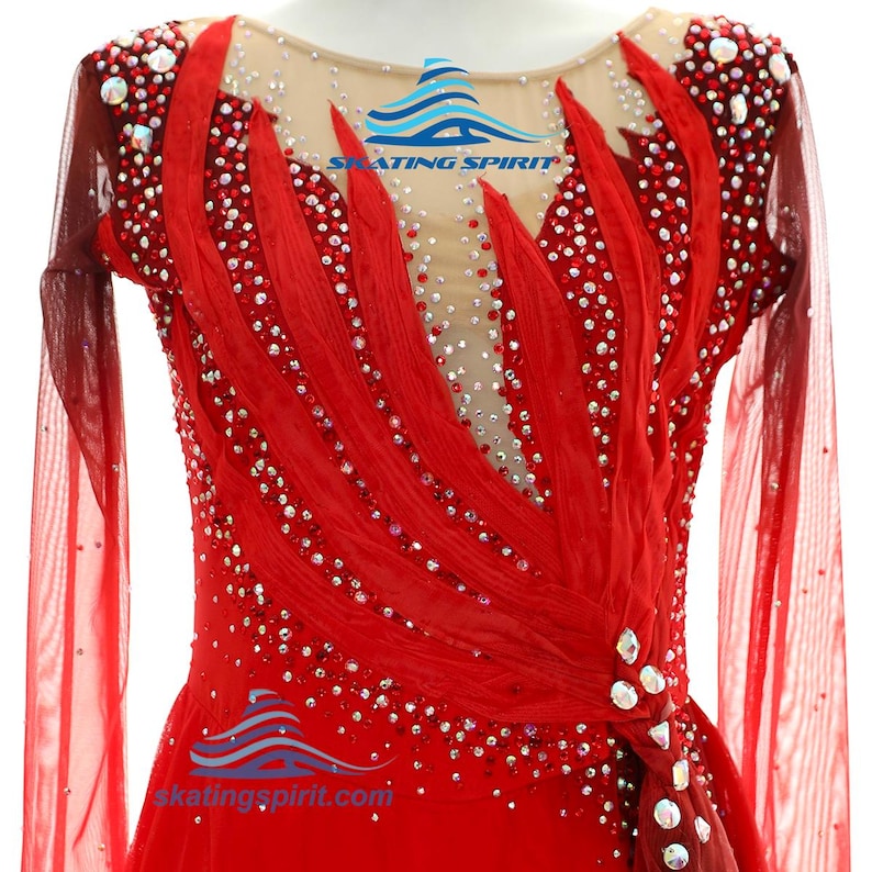 Peut inclure: Une robe de patinage rouge &agrave; manches longues avec un d&eacute;collet&eacute; et un empi&egrave;cement de corsage en maille couleur chair. Le v&ecirc;tement est richement orn&eacute; de nombreux cristaux rouges et transparents, avec des accents de tissu rouge superpos&eacute;s.