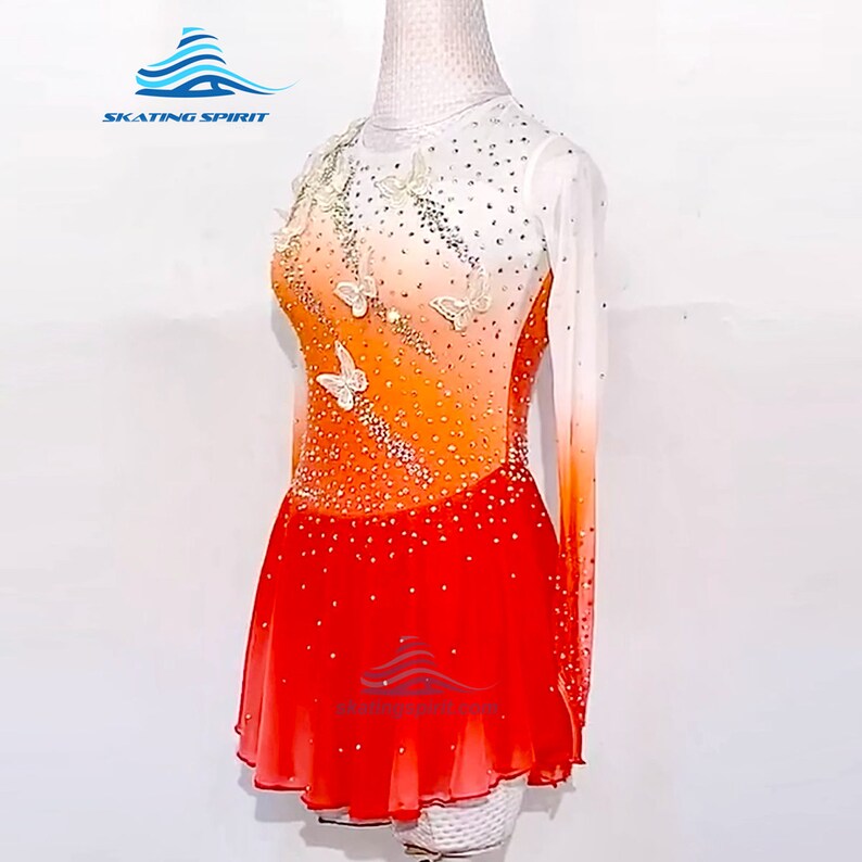 May include: A figure skating dress with a white, orange, and red ombre design. The dress has long sleeves and a skirt with a scalloped hem. The bodice is decorated with white butterflies and rhinestones.