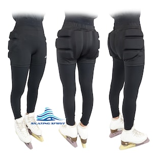 May include: Black figure skating pants with padded hips and a logo that says "SKATING SPIRIT". The pants are worn by a person wearing white figure skates.