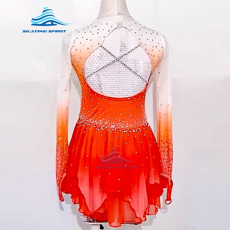 May include: Orange and white figure skating dress with long sleeves and a criss-cross back design. The dress is decorated with rhinestones and has a gradient effect.