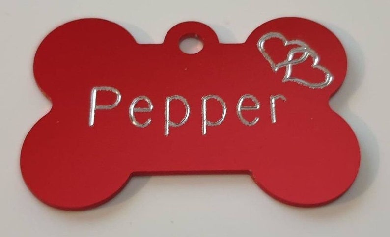 May include: Red bone-shaped dog tag with a silver inscription that reads "Pepper" and two silver hearts.