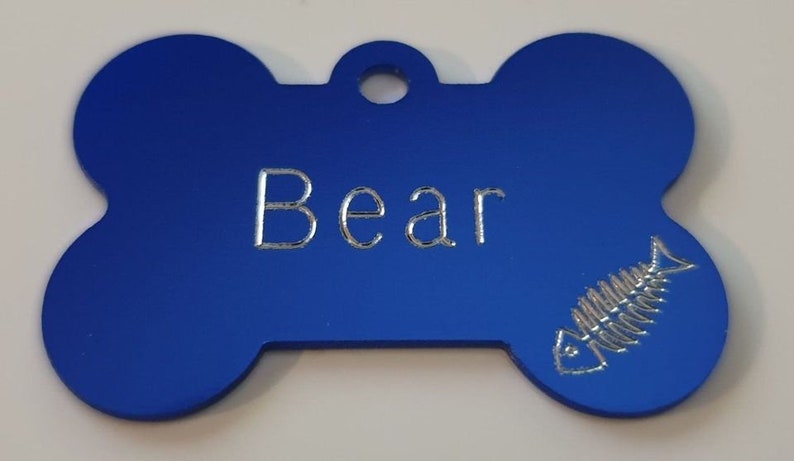 May include: Blue bone-shaped dog tag with the name "Bear" engraved in silver lettering and a silver fishbone design.