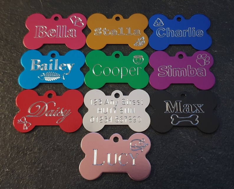 May include: Ten personalized bone-shaped dog tags in various colors, including red, blue, green, purple, black, gold, silver, and pink. Each tag features a different name, such as Bella, Stella, Charlie, Bailey, Cooper, Simba, Daisy, Max, and Lucy. Some tags also include additional details like a paw print, a bone, or a fish.
