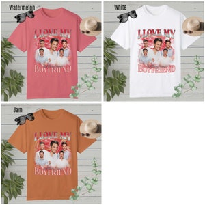 May include: Three t-shirts with the text "I Love My Boyfriend" in pink, white, and orange. The shirts feature a collage of photos of a boy band.