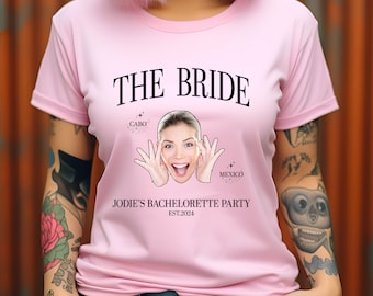 Könnte beinhalten: Pinkes T-Shirt mit dem Text "THE BRIDE" in Schwarz. Das Shirt zeigt außerdem ein Foto einer Frau mit dem Text "CABO" und "MEXICO" über ihrem Kopf. Der Text "JODIE'S BACHELORETTE PARTY EST. 2024" befindet sich unter dem Foto.
