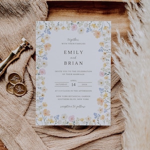 May include: A wedding invitation with floral border, featuring the names "Emily and Brian." The invitation includes the date, time, and location: New York Botanical Garden. The invitation is on a wooden tray with a beige fabric and decorative elements.