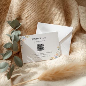 May include: A white RSVP card with floral accents and the text "KINDLY RSVP" and "By March 14, 20XX". Includes a QR code and website address. Accompanied by a white envelope, all on a textured beige surface.