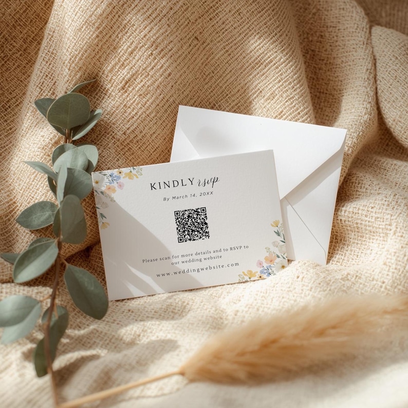 May include: A white RSVP card with floral accents and the text "KINDLY RSVP" and "By March 14, 20XX". Includes a QR code and website address. Accompanied by a white envelope, all on a textured beige surface.