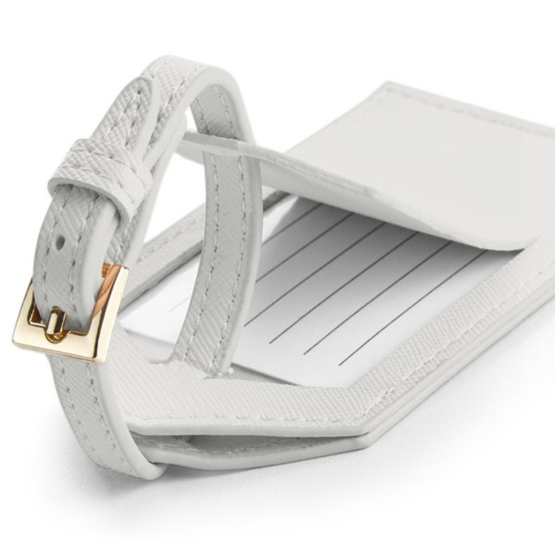 May include: White leather luggage tag with a gold metal buckle and a clear window for writing information.
