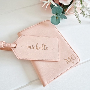 May include: A pink passport holder with a matching luggage tag. The luggage tag has the name "michelle" written on it in gold lettering. The passport holder has the initials "MG" in gold lettering.