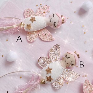 Peut inclure: Deux baguettes de f&eacute;e en feutrine &eacute;tiquet&eacute;es A et B, chacune avec un visage beige aux yeux ferm&eacute;s et sourire brod&eacute;s, un chignon rose avec un bandeau dor&eacute;, un corps en feutrine blanche avec deux &eacute;toiles dor&eacute;es paillet&eacute;es et des ailes roses.