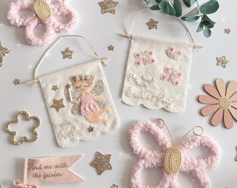 May include: A collection of whimsical fairy-themed decorations. Includes pink felt butterfly and flower shapes, glittery gold stars, and felt banners with fairy and butterfly designs. One banner reads "Find me with the fairies."