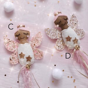 Peut inclure: Deux baguettes de f&eacute;e en feutrine &eacute;tiquet&eacute;es C et D, chacune repr&eacute;sentant une f&eacute;e &agrave; la peau brune avec un chignon rose, les yeux ferm&eacute;s et une robe blanche. Elles ont des ailes paillet&eacute;es dor&eacute;es et roses, deux &eacute;toiles dor&eacute;es et des franges roses.