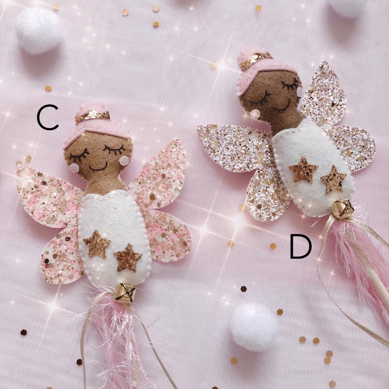 Peut inclure: Deux baguettes de f&eacute;e en feutrine &eacute;tiquet&eacute;es C et D, chacune repr&eacute;sentant une f&eacute;e &agrave; la peau brune avec un chignon rose, les yeux ferm&eacute;s et une robe blanche. Elles ont des ailes paillet&eacute;es dor&eacute;es et roses, deux &eacute;toiles dor&eacute;es et des franges roses.