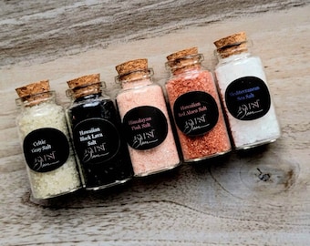 May include: Five small glass bottles filled with different types of salt, including Celtic Gray Salt, Hawaiian Black Lava Salt, Himalayan Pink Salt, Hawaiian Red Alaea Salt, and Mediterranean Sea Salt. Each bottle has a cork stopper and a black label.