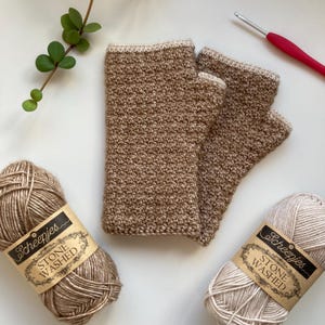 Peut inclure: Deux paires de mitaines en crochet en fil beige et blanc. Le fil est étiqueté "Stone Washed" et "Scheepjes".