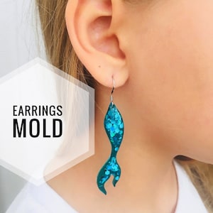 May include: Teal glitter mermaid tail earrings. The earrings are hanging from a person's ear. The text "EARRINGS MOLD" is visible in the image.