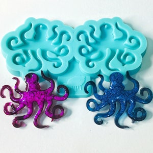 May include: A light blue silicone mold with two octopus-shaped resin castings. One octopus is a vibrant magenta, the other is a deep blue with a textured pattern. The mold is designed for crafting.