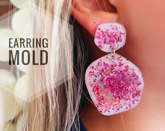 Könnte beinhalten: Ein Paar rosa und weiße Harzohrringe mit gepressten Blumen. Die Ohrringe sind sechseckig und haben ein baumelndes Design. Die Ohrringe werden von einer Person getragen.
