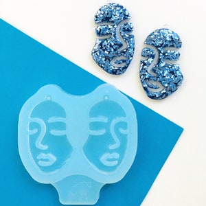 Può includere: Due orecchini astratti a forma di viso con glitter blu e uno stampo in silicone azzurro. Gli orecchini hanno un design ritagliato e un piccolo foro per appenderli. Lo stampo ha due forme di viso.