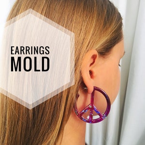 Può includere: Un paio di orecchini a forma di segno della pace realizzati in resina con una finitura viola e iridescente. Gli orecchini sono mostrati sull'orecchio di una modella. Il testo "EARRINGS MOLD" è visibile nell'immagine.