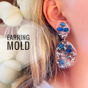 K&ouml;nnte beinhalten: Ein Paar transparente Harzohrringe mit gepressten blauen Blumen und silbernem Glitzer. Die Ohrringe sind tropfenf&ouml;rmig und rund. "EARRING MOLD" steht in wei&szlig;er Schrift auf wei&szlig;em Hintergrund.