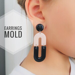 May include: Black and blush pink resin earrings with a geometric U-shape design. The earrings are shown on a person's ear. "EARRINGS MOLD" is written in white text on a white background.